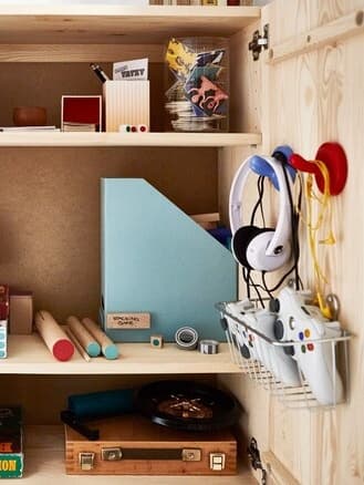 A IVAR pine shelving unit with doors used to store gaming accessories, magazine file and colouring accessories.