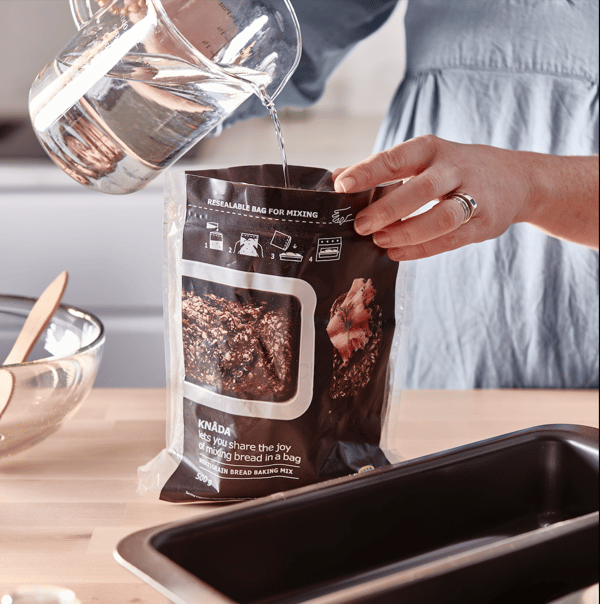 A jug pours water into a container to prepare the mixture of homemade bread dough