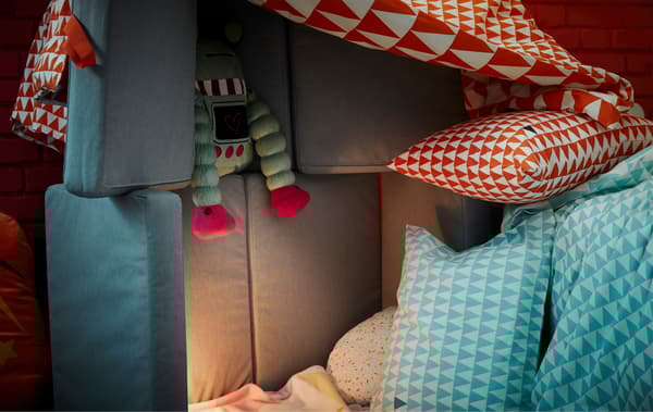 A jumble of bedsheets, cushions, soft toys and a foldable mattress created as a children’s fort.