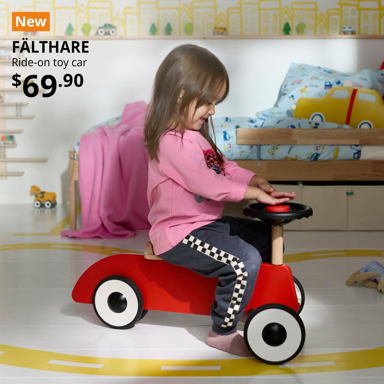 A kid on a red FÄLTHARE ride-on toy car in the children's bedroom setting. A orange tag with white text that reads "New", followed by black text overlay image that reads, "FÄLTHARE, Ride-on toy car, $69.90". 