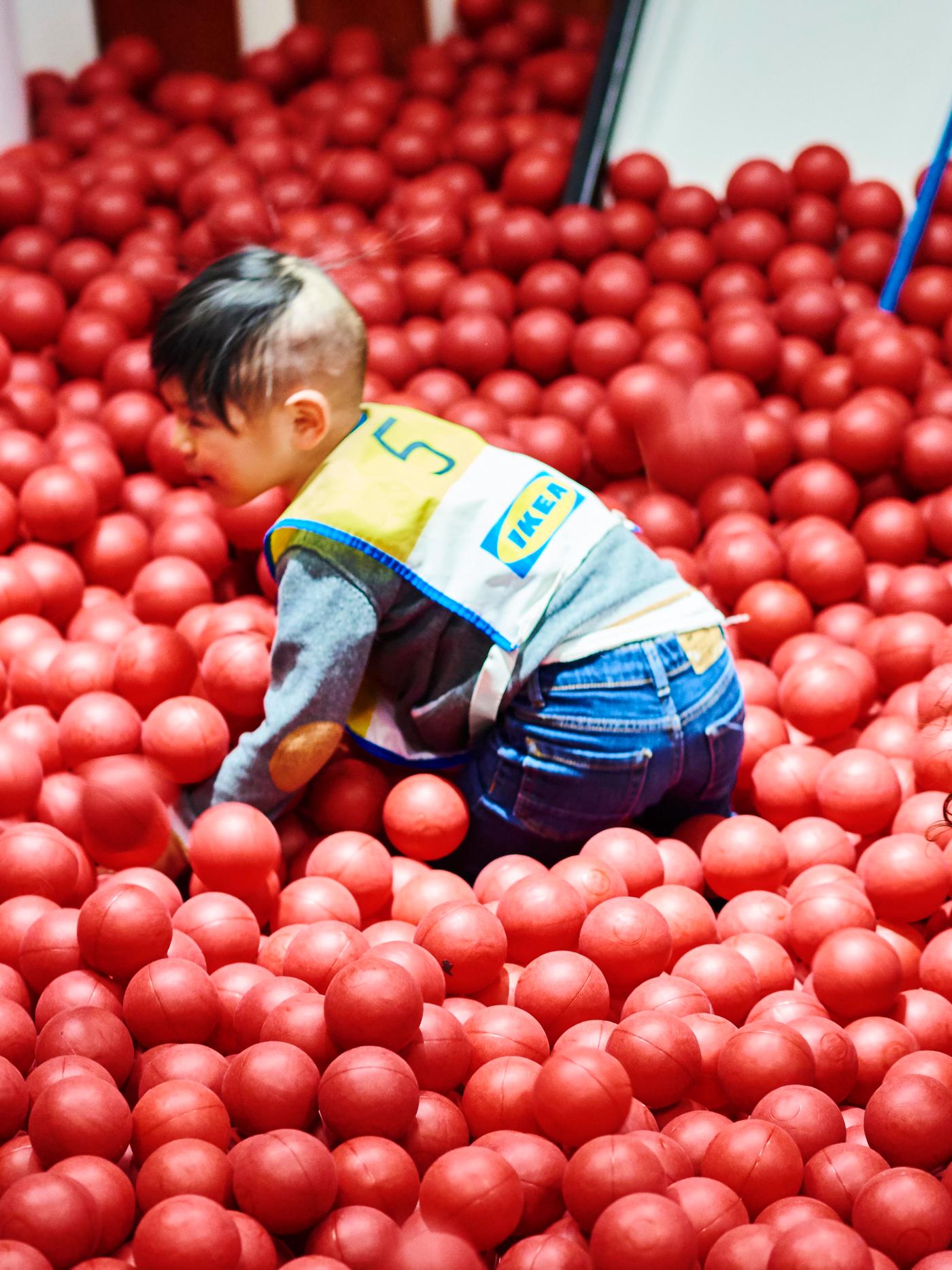 A kid playing in a red ball pit