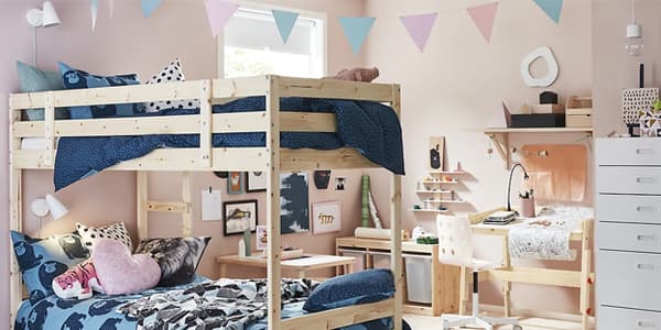 A kid’s bedroom with pink walls, bunk bed with blue bedding, and light wood desk and storage.