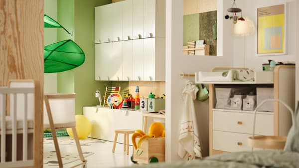 A kids room partially seperated with a wall. One side has SMÅSTAD cupboards and toys. The other has a baby changing area.
