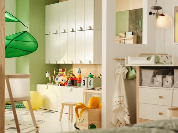 A kids room partially seperated with a wall. One side has SMÅSTAD cupboards and toys. The other has a baby changing area.