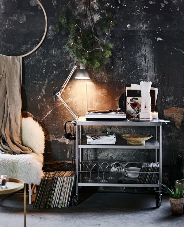 A kitchen cart used as a shelving unit with a record player, work lamp and martini glasses.