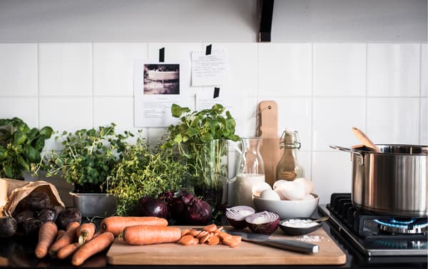 A kitchen counter top and wooden cutting board piled high with fresh vegetables and herbs.