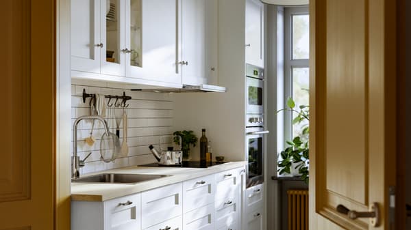 A kitchen has drawers and wall cabinets with white ENKÖPING fronts and a nickel-plated HULTARP rail with hooks on the wall.