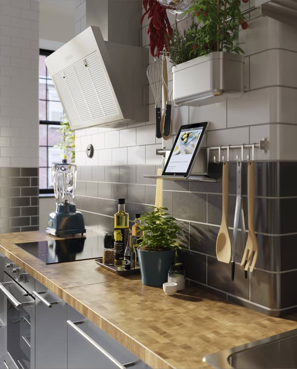 A kitchen in stainless steel, a wood worktop, fresh herbs and a wall-mounted rail with a tablet on a tablet stand.