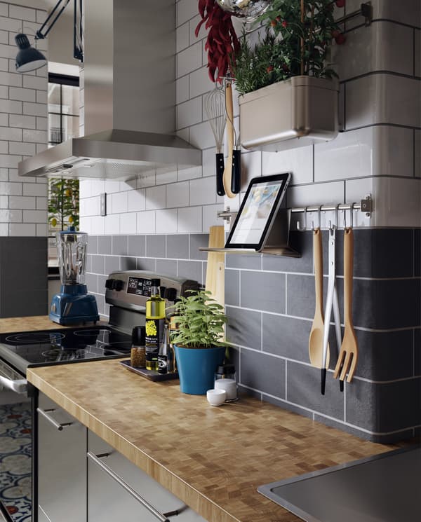 A kitchen in stainless steel, a wood worktop, fresh herbs and a wall-mounted rail with a tablet on a tablet stand.