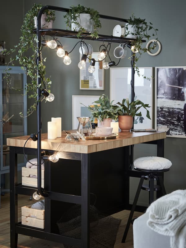 A kitchen island with rack decorated with a black lighting chain and trailing leafy green plants in white plant pots.