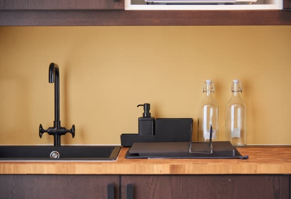 A kitchen setting featuring a black tap and sink, chopping board and glass bottles on a wooden countertops.