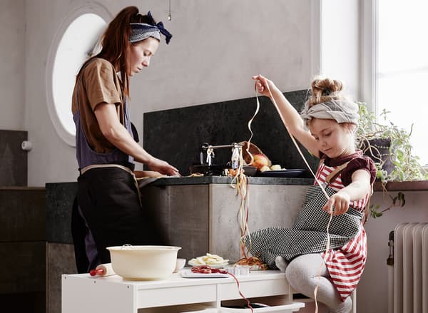 A kitchen where a mom is kneading dough while her little daughter is fixing a garland.