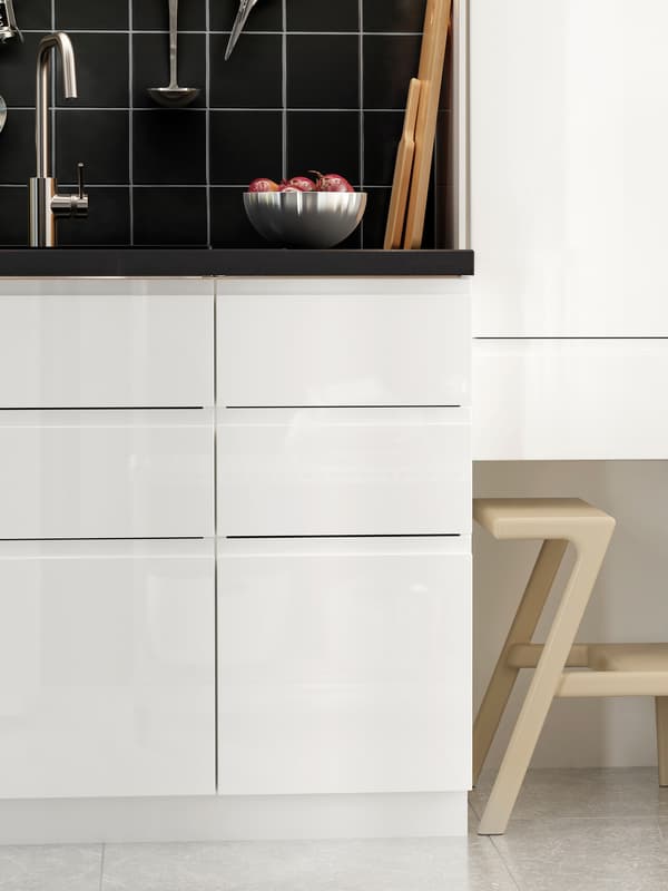 A kitchen with a black stone-effect worktop, white drawer fronts and a white high cabinet with a step stool below.