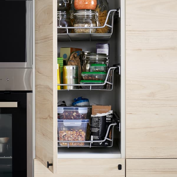 A kitchen with a high cabinet in a light ash effect door that is open to show wire baskets, food containers and more inside.