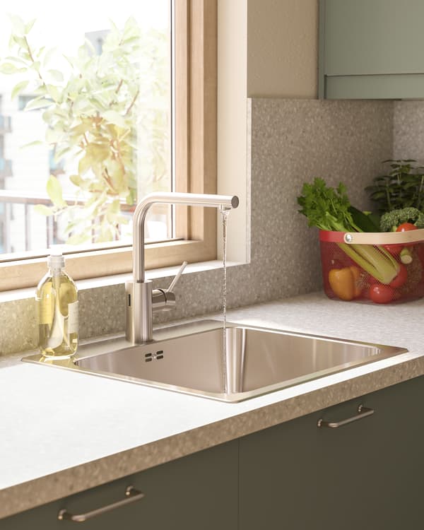 A kitchen with a stainless steel-coloured kitchen mixer tap with a sensor on the side, water is running from the tap.