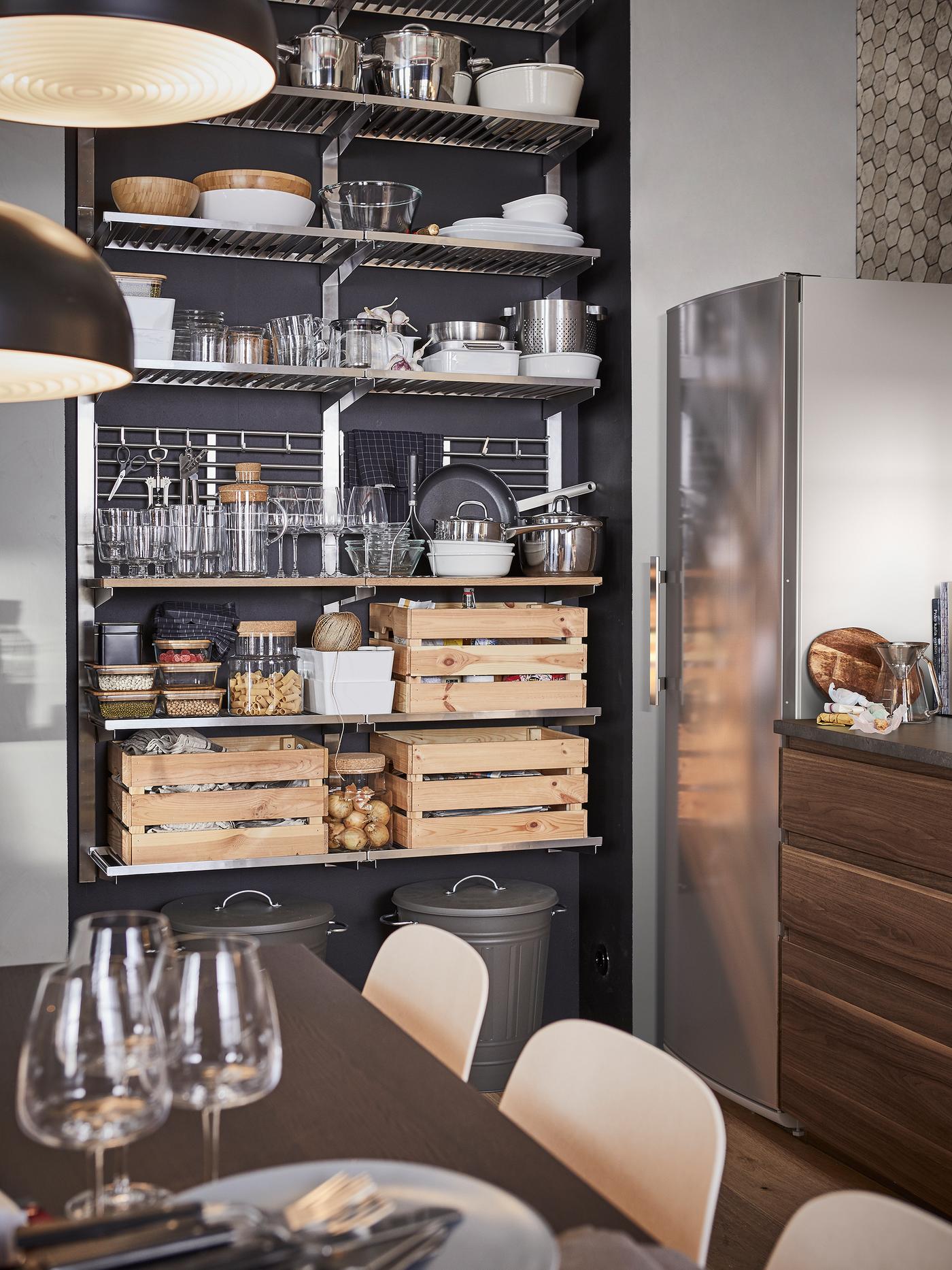 A kitchen with a stainless steel open storage shelving unit storing containers, tableware and three boxes in pine.