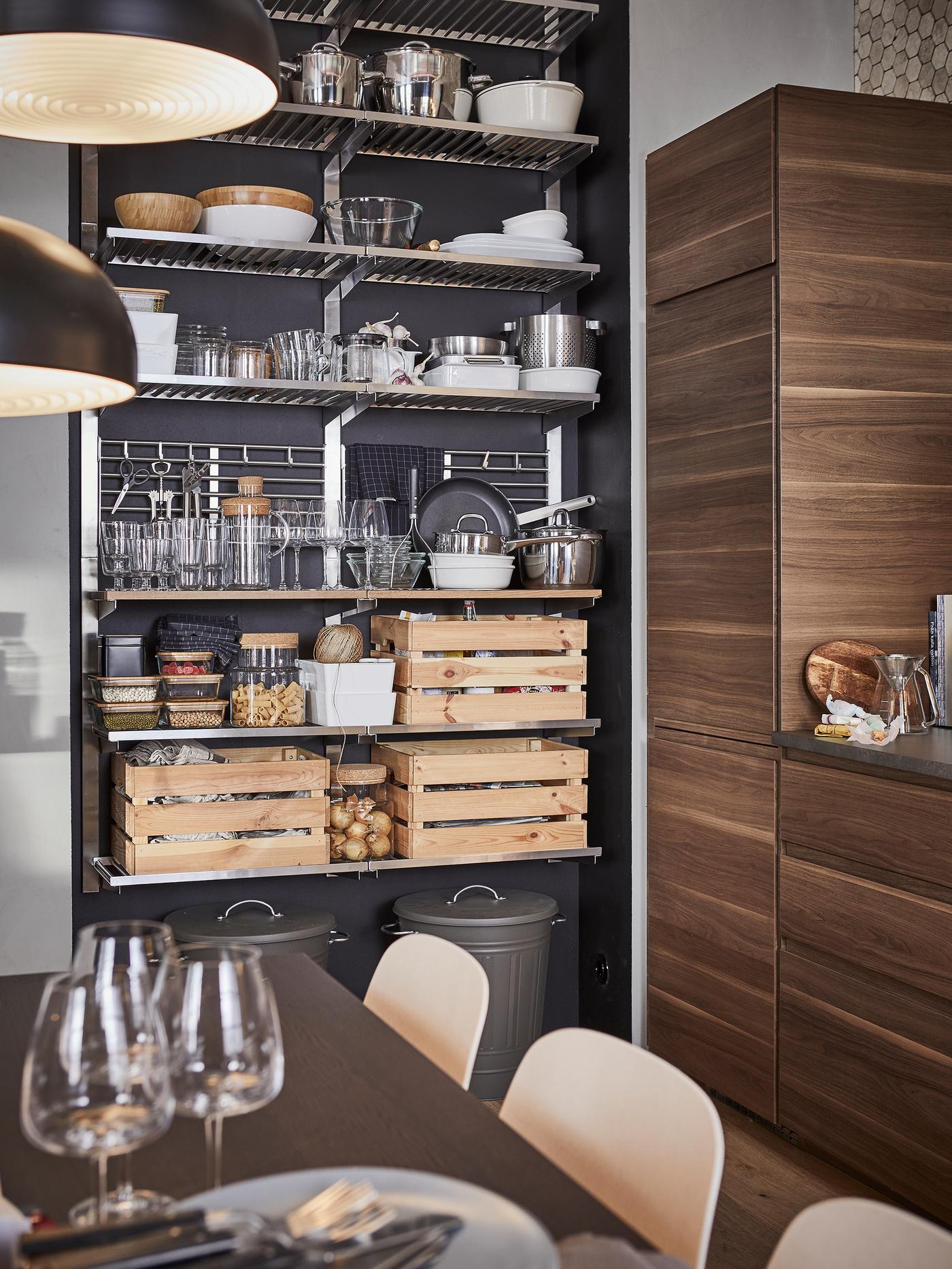 A kitchen with a stainless steel open storage shelving unit storing containers, tableware and three boxes in pine.