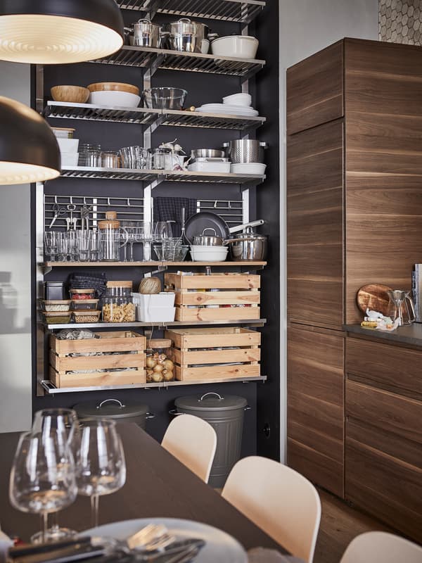 A kitchen with a stainless steel open storage shelving unit storing containers, tableware and three boxes in pine.