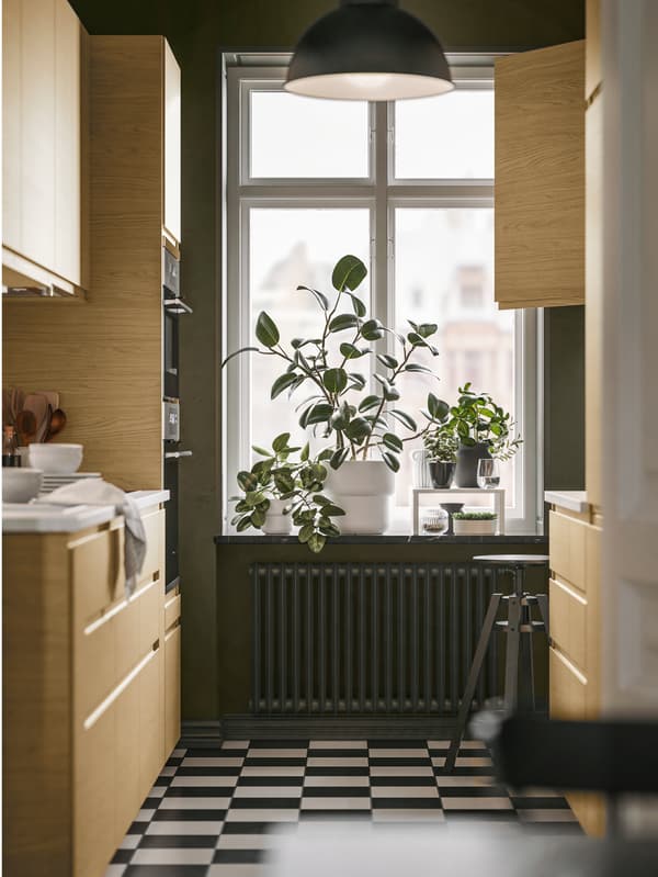 A kitchen with a tall window has several base and wall cabinets with VOXTORP fronts with oak effect and integrated handles.
