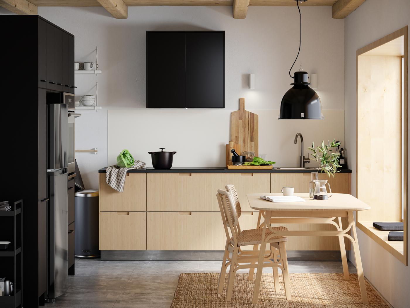 A kitchen with a VOXLÖV dining table in light bamboo with two chairs and a SVARTNORA pendant lamp in black hanging above.