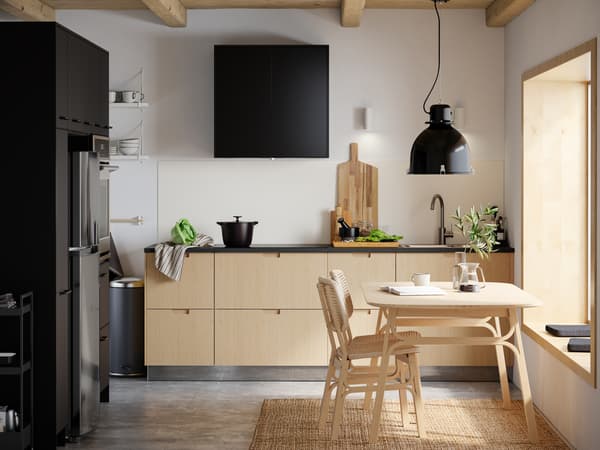 A kitchen with a VOXLÖV dining table in light bamboo with two chairs and a SVARTNORA pendant lamp in black hanging above.