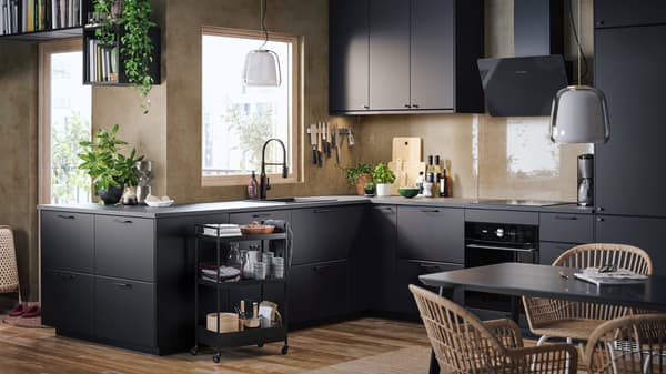 A kitchen with beige walls, wooden floors, KUNGSBACKA kitchen fronts in anthracite and a trolley with kitchen accessories.