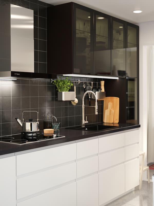 A kitchen with black wall cabinets with high glass doors, white drawers and a quartz anthracite mineral-effect worktop.