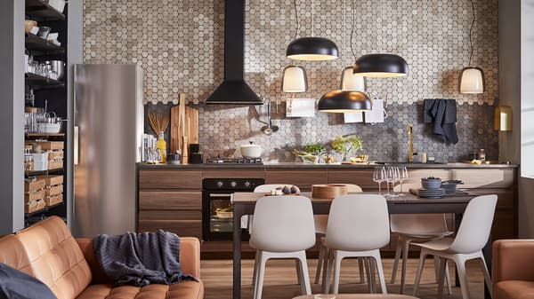 A kitchen with cabinets in dark brown walnut-effect wood, three black pendant lamps, a dark brown table and six chairs.