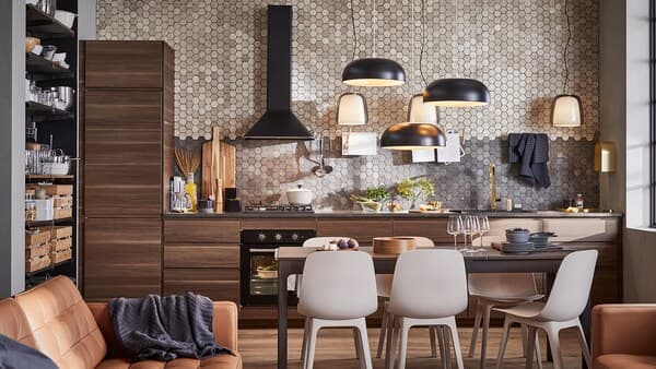 A kitchen with cabinets in dark brown walnut-effect wood, three black pendant lamps, a dark brown table and six chairs.