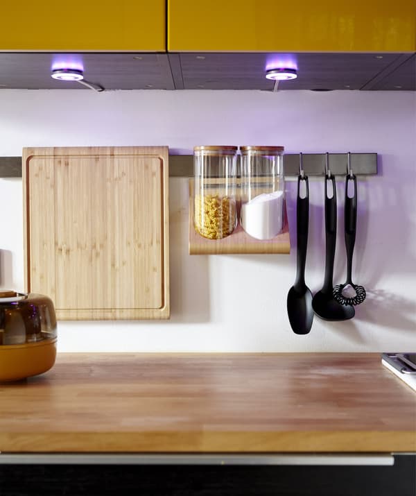 A kitchen with cupboard spotlights and a hanging utensils rack.