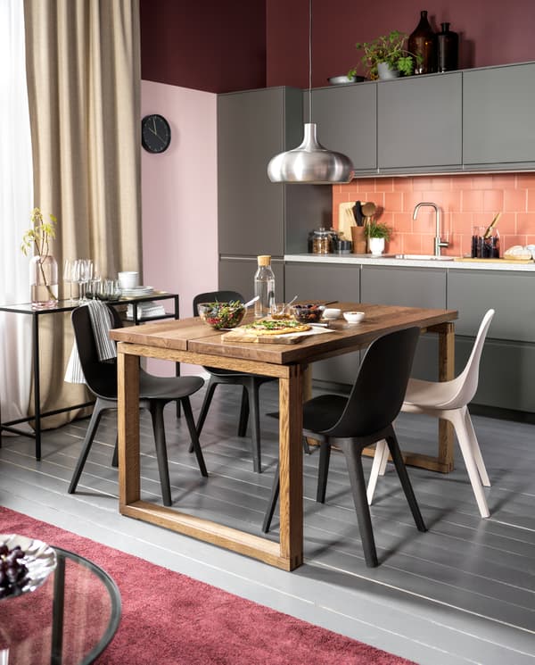 A kitchen with dark grey fronts, a table in oak veneer, chairs in anthracite/white and an aluminium-coloured pendant lamp.