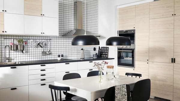 A kitchen with doors in white and light ash effect, two black pendant lamps, a white table and black chairs.