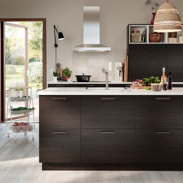 A kitchen with drawers and doors in dark brown ash effect, a pendant lamp shade made from seagrass and a white trolley.