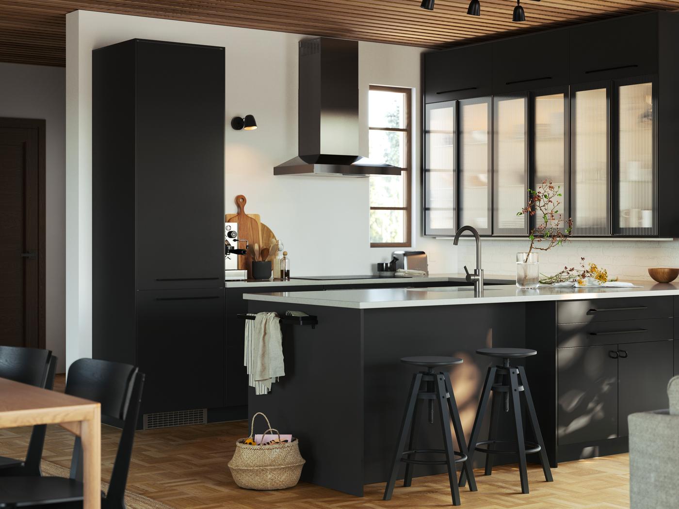 A kitchen with FÖRBÄTTRA panels, cabinets with HEJSTA glass doors in anthracite/reeded glass and DALFRED bar stools in black.