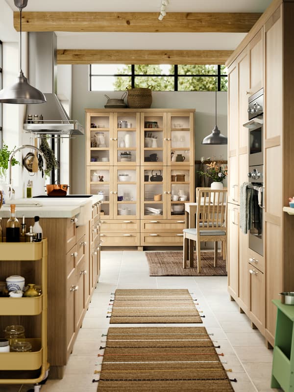 A kitchen with FORSBACKA fronts in oak veneer, a glass-door cabinet and a SÄLJAN worktop with white stone effect/laminate.