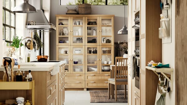 A kitchen with FORSBACKA fronts in oak veneer, a glass-door cabinet and a SÄLJAN worktop with white stone effect/laminate.