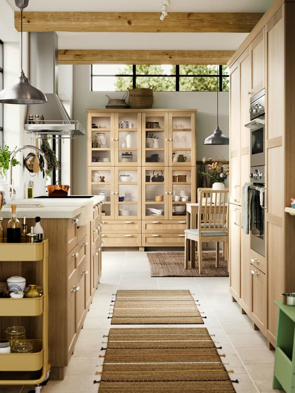A kitchen with FORSBACKA fronts in oak veneer, a glass-door cabinet and a SÄLJAN worktop with white stone effect/laminate.
