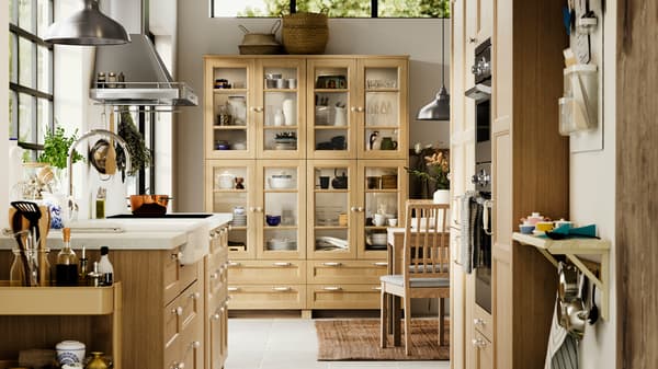A kitchen with FORSBACKA fronts in oak veneer, a glass-door cabinet and a SÄLJAN worktop with white stone effect/laminate.