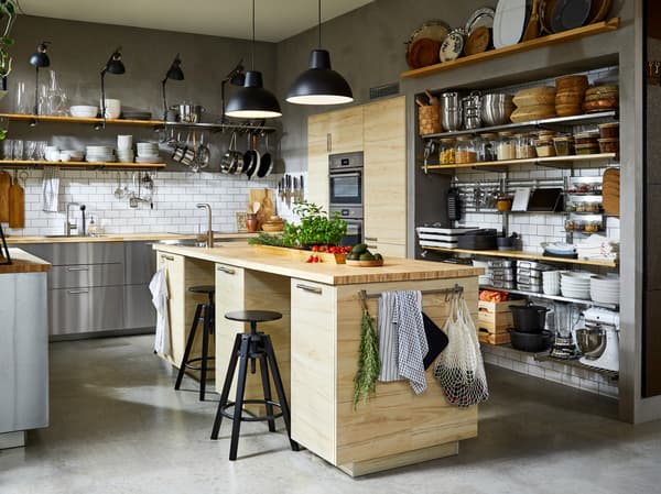 A kitchen with fronts in stainless steel, two black pendant lamps and a spacious kitchen island with two black bar stools.
