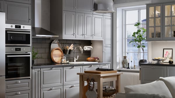 A kitchen with grey tiles and white walls has grey BODBYN fronts with bevelled panels and a kitchen island in the middle.