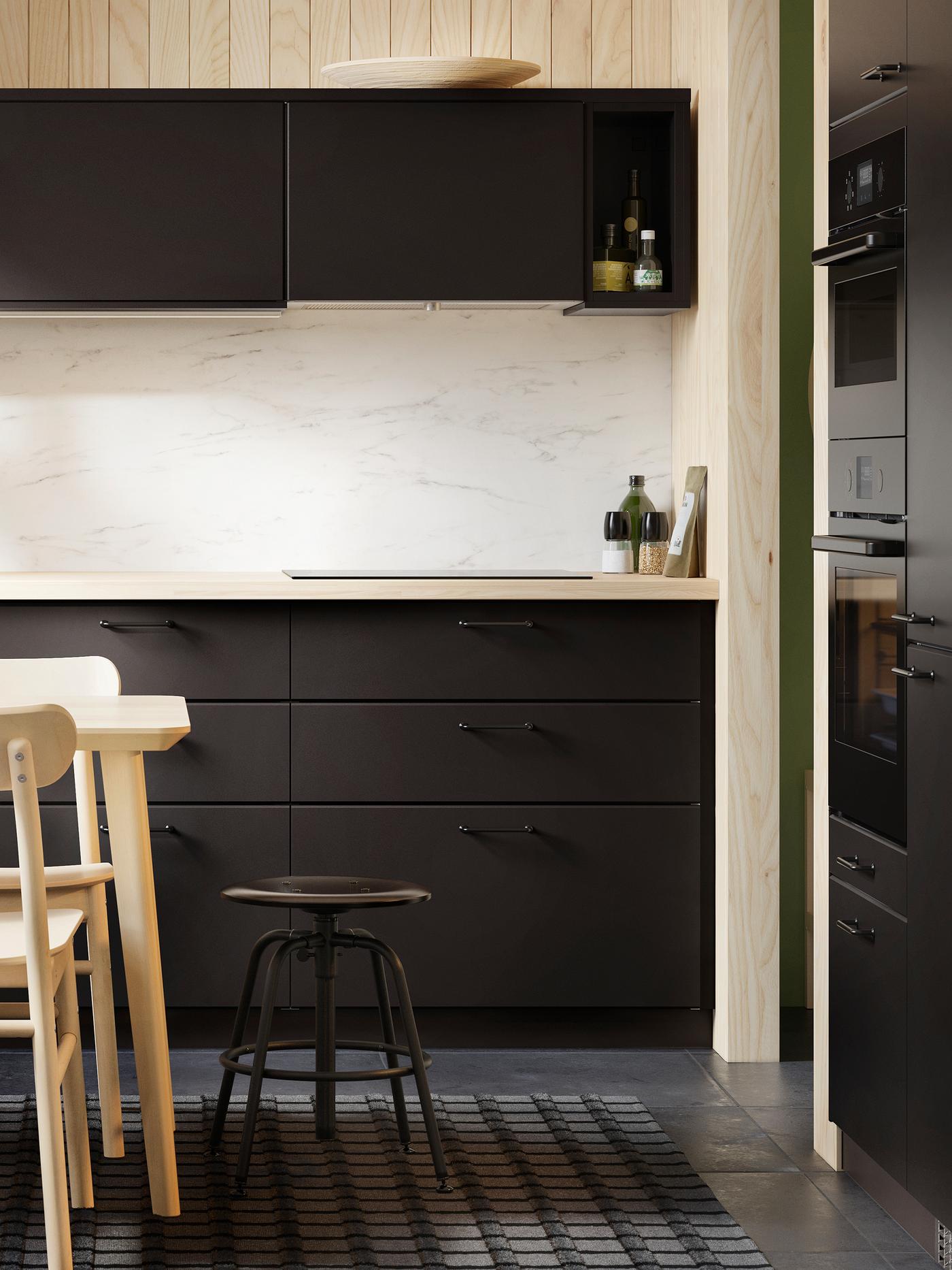 A kitchen with KUNGSBACKA anthracite cabinet doors and drawer fronts, a marble effect splashback and a black stool.