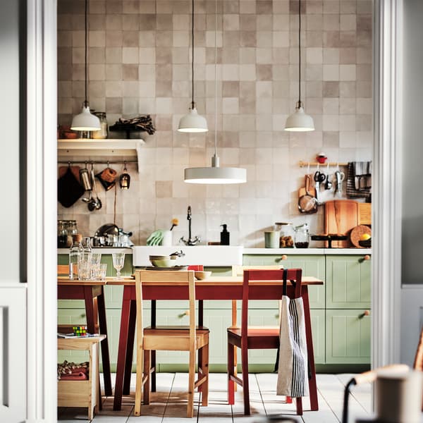 A kitchen with light green STENSUND drawer fronts and two PINNTORP tables surrounded by PINNTORP chairs.