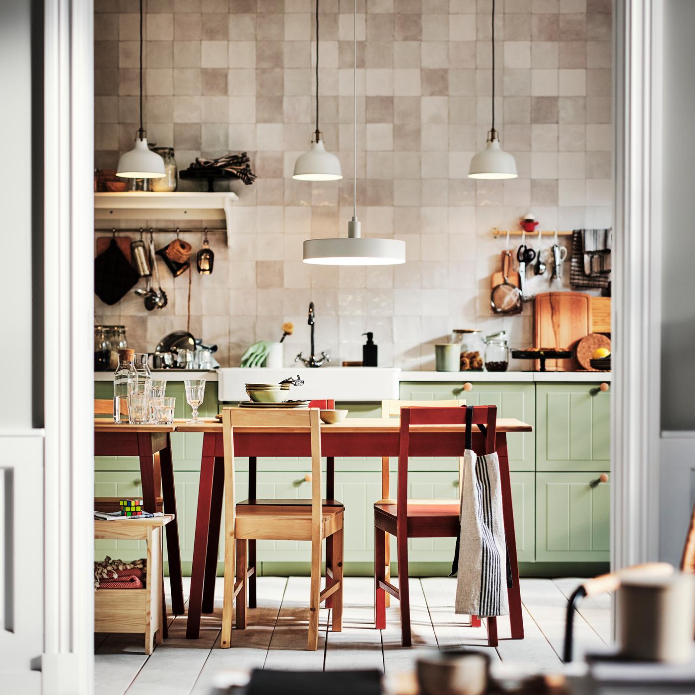 A kitchen with light green STENSUND drawer fronts and two PINNTORP tables surrounded by PINNTORP chairs.