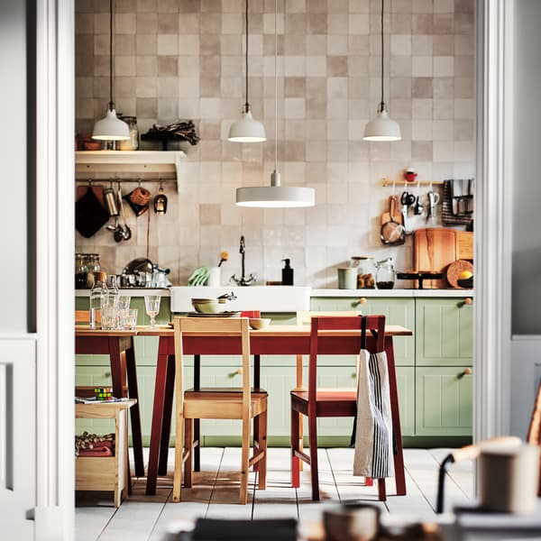 A kitchen with light green STENSUND drawer fronts and two PINNTORP tables surrounded by PINNTORP chairs.