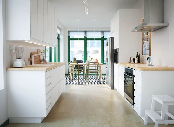 A kitchen with sleek white VOXTORP doors and PINNARP worktop in ash. A dining area can be glimpsed in the background. 