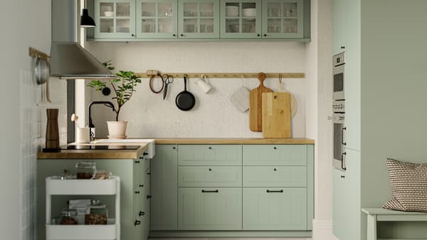 A kitchen with STENSUND light green fronts, a GRUNDAD induction hob in black and a MATTRADITION wall-mounted extractor hood.