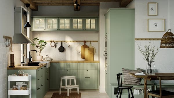A kitchen with STENSUND light green fronts, a GRUNDAD induction hob in black and a MATTRADITION wall-mounted extractor hood.