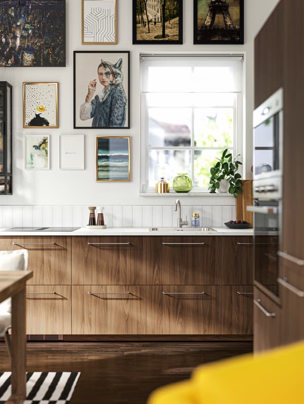 A kitchen with TISTORP fronts with a brown walnut effect, a dark wood floor and some posters on the wall next to a window.
