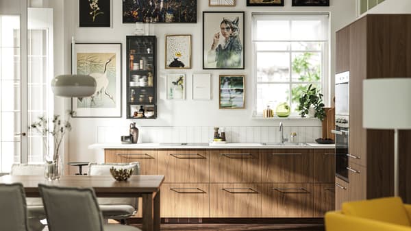 A kitchen with TISTORP fronts with a brown walnut effect, a dark wood floor and some posters on the wall next to a window.
