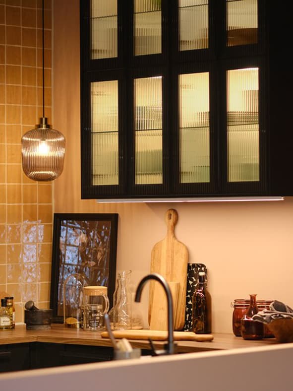 A kitchen with wall cabinets with glass doors and lighting inside, plus pendant lamps over the worktop and extendable table.
